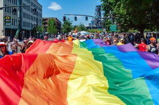 a large rainbow flag is held by many walking in a city street during a pride parade