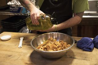 Oil pouring into a bowl of freshly cleaned mushrooms.