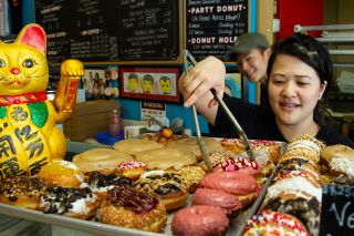 person using tongs to select a doughnut from a tray