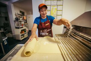 a baker sprinkles flour over a large sheet of dough