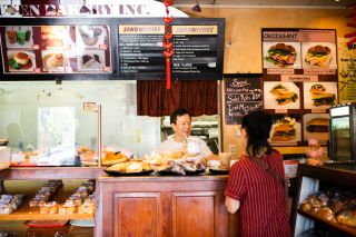 A man behind a bakery counter serves a customer