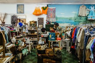 A thrift store is st\uffed with racks of clothing and accessories. An orange tutu hangs from a back wall.