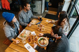 a group of four around a wooden table enjoy draft beers and pub food