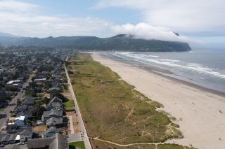 a view from high above the Seaside Promenade on a partly cloudy day, with homes on the left, the beach to the right and a wooded hill in the distance