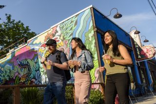 walking toward the sun, three people pass a colorful mural painted on the side of a building