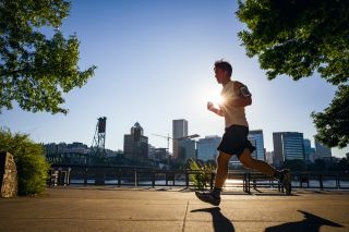 bright afternoon sun blocked by person running on river side path with view of downtown buildings and bridge