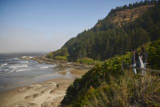 people at viewpoint looking over beach and incoming tide with a low fog and blue sky