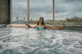 A woman relaxes in a hot tub with a view of Willamette River bridges in the background.