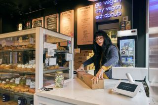 a woman at a counter closes the lid on a box of doughnuts