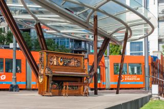 a piano that is playfully painted sits at a streetcar stop in an urban setting