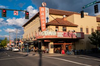 street view of an old movie house in a busy shopping district, people sit out under the marquee in a sunny spring day