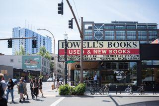 people cross the street in front of a huge white and red marquee with the words “Powell’s Books Used & New Books” in black letters