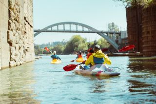 a view from river as people kayak through the locks in Oregon City with view of the old bridge