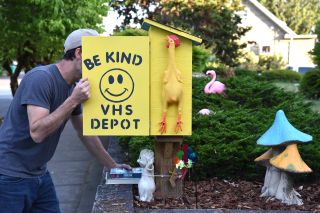 a person opens a bright yellow box in a yard filled with garden ornaments