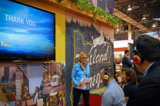 a woman in a blue shirt presents to a group of viewers in front of a screen with Travel Portland logo