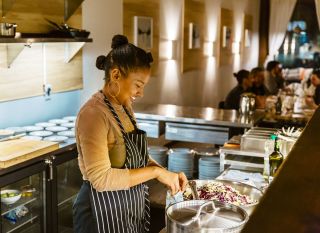 Chef Amabebe preparing dishes for Nigerian pop-up dinners in a kitchen.