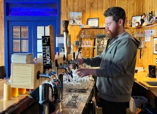 A man wearing a gray hoodie pours a glass of beer from a beer tap at 13th Moon Gravity Well.