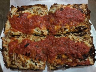 Four pizza slices dressed with marinara sauce rest on a metal plate lined with parchment paper.