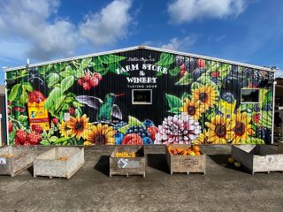 a brightly colored mural depicting berries, flowers and a humming bird painted on the side of a farm store building