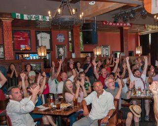 a crowd of people sitting at tables and cheering at Kells Brew Pub