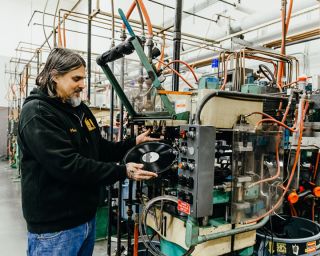 man holding a newly pressed record in front of pressing machine