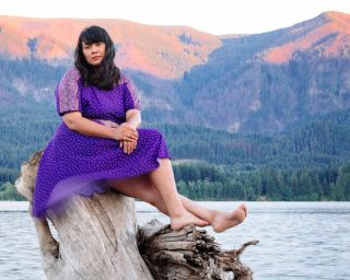 Katherine Paul sits on tree stump in front of mountain and lake vista