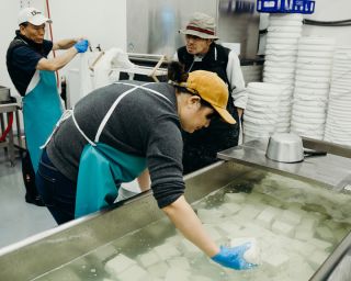 woman setting blocks of white tofu in large vat of water