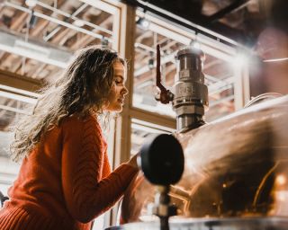 woman in front of copper still making spirits