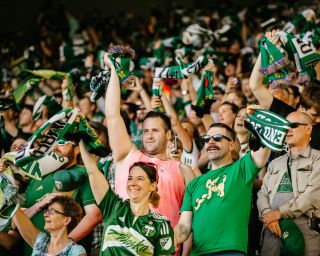 A packed crowd of soccer fans wave green Timbers scarves