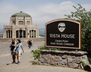 visitors walk away from the vista house, past a sign that says "Vista House"