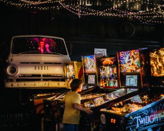 a child plays pinball at one of several glowing pinball machines