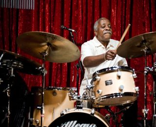 a man playing drums on stage in front of a red curtain