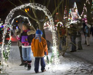 Families walking in the snow enjoying the holiday lights on houses, trees and arches erected over the sidewalks.