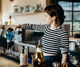 a bartender behind the bar pouring drinks from a blue bottle