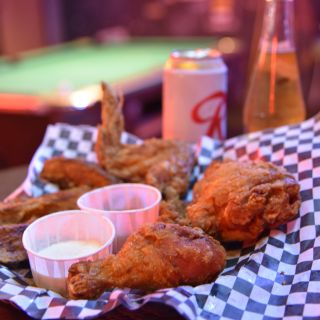 an order of appetizing fried chicken with two beers and a pool table in the background