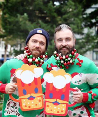 two men wearing Christmas decorations in their beards hold up 2-D depictions of beer mugs