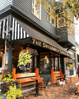 Exterior of a coffeeshop with two benches, hanging plants and a striped awning