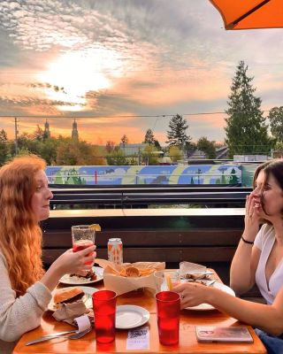 two people sit at an outdoor patio table beneath a vibrant sky