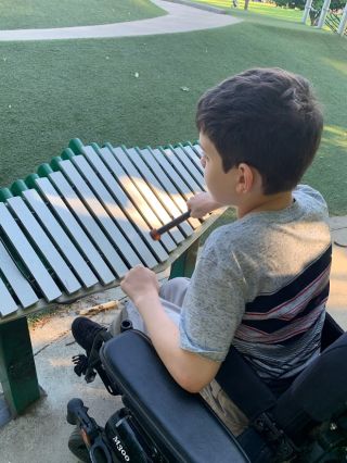 A child in a wheelchair plays a xylophone at a park