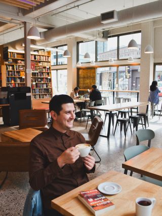 a person in the foreground drinks coffee at a cafe in a book store