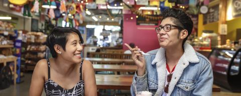 Two smiling people sit at a wooden table in a brightly decorated interior