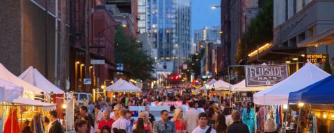 a twilight street filled with people browsing tents with items on display