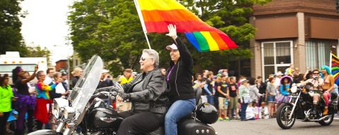 Two pride parade participants on a motorcycle with a rainbow pride flag