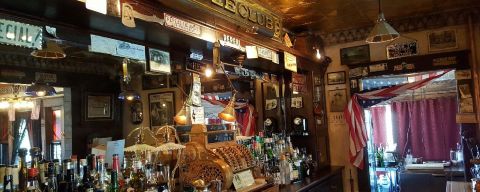 an old, golden cash register on a bar countertop with bottles and a large mirror on the back wall