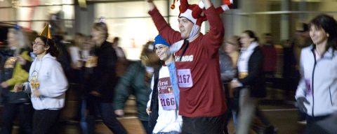 a man in a joker hat is among a crowd of people running in a fun run for new year\'s eve