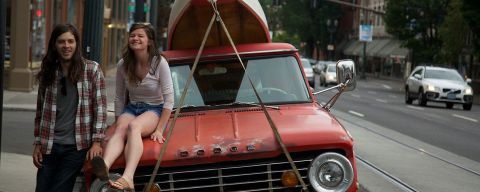 two people next to an orange truck with a canoe strapped to the top