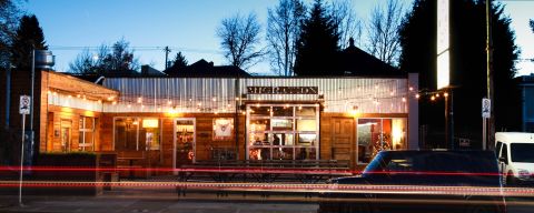 A well-lit building at dusk has outdoor seating and a sign out front that reads, \"Migration.\"