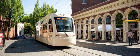 Light rail train car driving past people shopping at an outdoor market