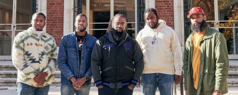 Five men stand in front of a set of marble steps leading up to a brick building