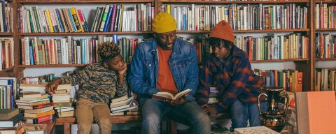 Three people sit and read a book at Mother Foucault\'s bookstore in front of a wall of books.